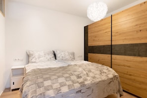 Ein Schlafzimmer mit einem Bett, einem Nachttisch, einem Holzschrank und einer weißen Deckenleuchte.