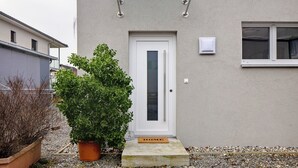 A house with a white door, a small potted plant, a doormat, and a glass awning above the door. - Apartment 'König' with Mountain View, Shared Terrace and Wi-Fi (Lustenau)