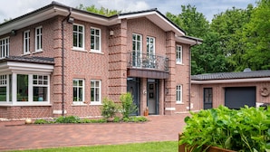A two-story brick house with a front porch, a garage, and a small garden. - Apartment Kronsberg with Sauna, Private Garden, Wi-Fi and Air Conditioning (Bösel)