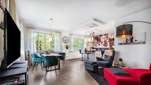 A modern living room with a red sofa, teal chairs, a dining area with a table, and a kitchen in the background. - Apartment Kronsberg with Sauna, Private Garden, Wi-Fi and Air Conditioning (Bösel)