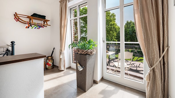 A room with a sliding glass door to an outdoor patio, a wooden drying rack, a wicker basket with a plant, and a small table with chairs. - Apartment Kronsberg with Sauna, Private Garden, Wi-Fi and Air Conditioning (Bösel)