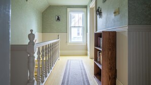 A hallway with a wooden railing, a window, and a bookshelf. - The 2,400 sq. ft. Plymouth Paddock near Road America, 4 bedrooms, 2.5 bathrooms  (Plymouth)