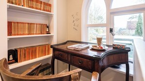 Eine gemütliche Leseecke mit einem Holztisch, Bücherregalen voller Bücher, einer Tasse Kaffee und Blick durch ein großes Rundbogenfenster.