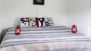 Un dormitorio con una cama, almohadas con banderas de Puerto Rico y dos farolillos rojos.