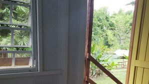 Una habitación con una silla blanca, un ventanal con vistas a la vegetación y una escalera de madera que da al exterior.