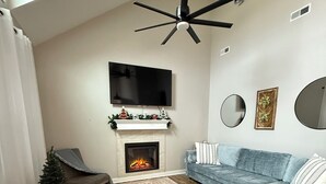 Un salon moderne avec une cheminée, un téléviseur fixé au mur et un ventilateur de plafond.