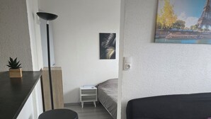 A modern room with a black sofa, a small bed, a desk with a chair, and a painting of the Eiffel Tower. - Le Cocoon / Free parking / Wifi (Belfort)