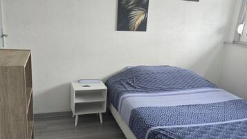 Une chambre à coucher comprenant un lit, une table de chevet, une armoire en bois et deux œuvres d’art accrochées au mur.