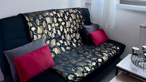 A living room with a black sofa adorned with gold leaf patterns, red and gray cushions, and a painting of the Eiffel Tower above. - Le Cocoon / Free parking / Wifi (Belfort)