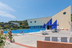 Area piscina con un edificio moderno, poltrona a sdraio e piscina.