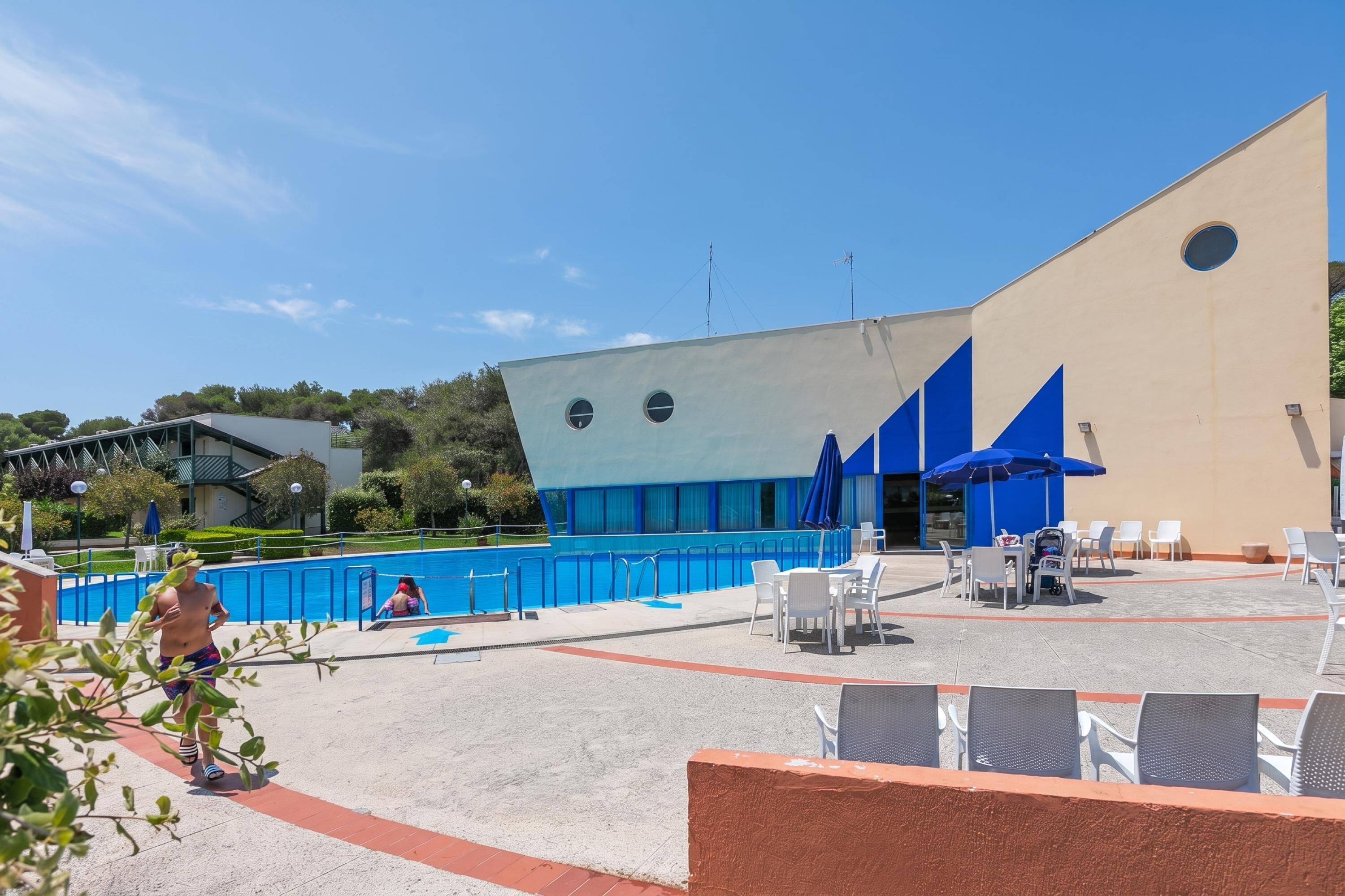 Ein Poolbereich im Freien mit einem modernen Gebäude, Sitzgelegenheiten und blauem Himmel.
