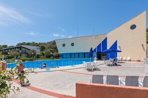 An outdoor swimming pool area with a modern building, seating, and a clear sky.