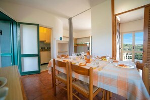 A dining area with a table set for four, chairs, a kitchen in the background, and a view through a window. - Alba Apartment 1 with Pool and Sea n.41, Otranto, Italy (Otranto)