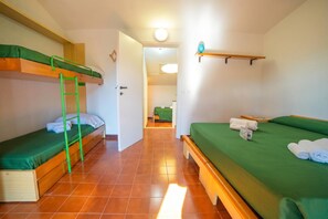 A room with bunk beds, a ladder, a green bedspread, and a hallway leading to another room.