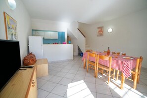 A compact living space with a kitchenette, a dining area with a checkered tablecloth, a TV, and a wooden bench.