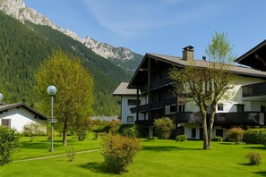 A multi-story building with balconies, surrounded by lush green lawns and a mountain backdrop.