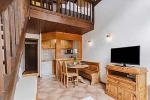 Puisesta ruokapöydästä ja tuoleista koostuva ruokailuryhmä, penkki, televisio puisen jalustan päällä sekä keittiö, jossa on puiset kaapit ja mikroaaltouuni.