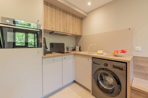 Une cuisine compacte équipée d’un four encastré, d’un lave-linge et d’une fenêtre donnant sur un espace verdoyant.