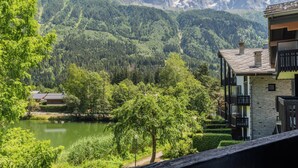 Vista de una montaña con un lago, un edificio con balcones y un camino que lleva a una casa.