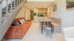 Un apartamento moderno con una escalera, una sala de estar con sofá y sillones, una zona de cocina y una mesa de comedor.
