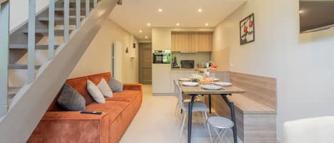 Un apartamento moderno con una escalera, una sala de estar con sofá y sillones, una zona de cocina y una mesa de comedor.