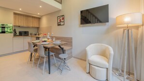 Una cocina moderna con armarios de madera, una mesa de comedor con sillas, un televisor de pantalla plana y una lámpara de pie.