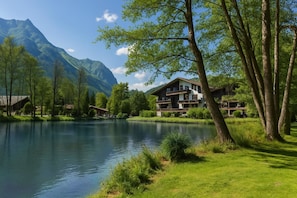 A lakeside hotel with a mountain backdrop, a grassy area, and a building with multiple balconies.