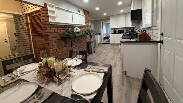 A modern kitchen with white cabinets, a brick accent wall, and a dining area set for a meal. - Newly Renovated Gem Fenced Backyard 2 Full Baths (Allen Park)