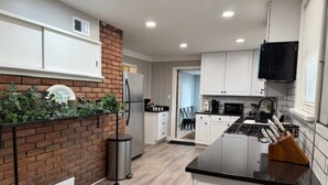 A modern kitchen with white cabinets, a black countertop, and a brick accent wall. - Newly Renovated Gem Fenced Backyard 2 Full Baths (Allen Park)