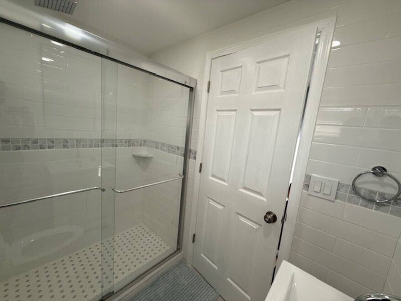 A bathroom with a glass shower enclosure, a white door, and a tiled wall.
