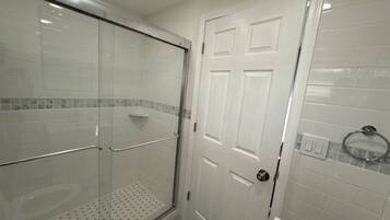 A bathroom with a glass shower enclosure, a white door, and a tiled wall.