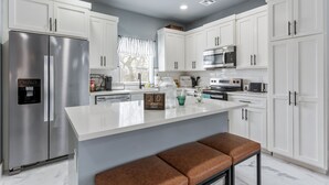 A modern kitchen with white cabinets, stainless steel appliances, and a central island with seating. - Modern Masterpiece in Downtown Tulsa-Sleeps 6 (Tulsa)