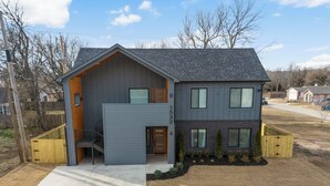 A two-story house with a grey exterior, a wooden front door, and a visible garage door. - Modern Masterpiece in Downtown Tulsa-Sleeps 6 (Tulsa)