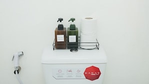 Inodoro blanco con secamanos, dos dispensadores de jabón y un rollo de papel higiénico.