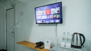 Habitación de hotel con televisor montado mostrando servicios de streaming, señal de Wi-Fi, cafetera y estante con control remoto.