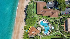 Luftaufnahme eines Resorts mit großem Pool, direkt am Strand und mehreren Gebäuden.