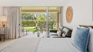 Ein Schlafzimmer mit einem großen Bett, einer Couch, einem Tisch und Blick auf einen Garten durch eine Schiebetür.
