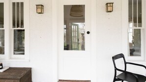 A white door with a green glass panel, two wall-mounted lanterns, and a black chair outside.