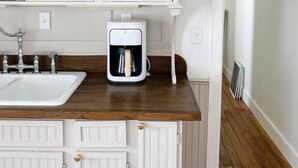 Une cuisine avec des meubles blancs, une machine à café posée sur le plan de travail et un évier.
