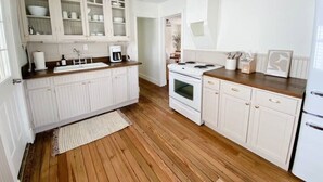 Une cuisine avec des meubles blancs, un plan de travail en bois, une cuisinière et un réfrigérateur.