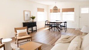 Un salon comprenant un canapé, une table basse, une table à manger avec des chaises, un meuble noir et un luminaire suspendu.