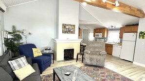 Amplia sala de estar con techo alto, chimenea, comedor y cocina con alacenas de madera.