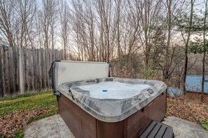 Ein Whirlpool in einem Garten mit Holzzaun und bodenbedeckenden Blättern.