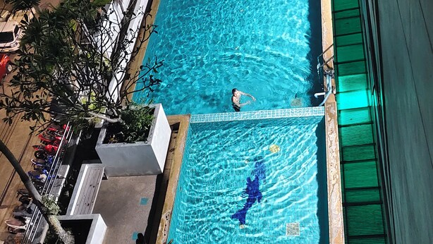A rectangular swimming pool with clear blue water, surrounded by a concrete deck and some greenery. - Cosy room like home, The Central Bangkok Station (Krung Thep Maha Nakhon)