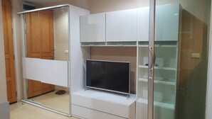A room with a sliding glass door closet, a flat-screen TV on a white stand, and a glass-fronted shelving unit. - Cosy room like home, The Central Bangkok Station (Krung Thep Maha Nakhon)