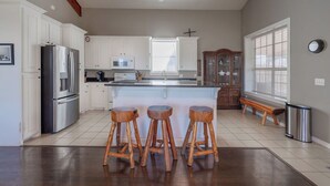 Une cuisine spacieuse avec des meubles blancs, un réfrigérateur en acier inoxydable, un four à micro-ondes et des tabourets en bois.