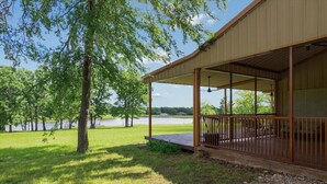 Un espace extérieur abrité, doté d’une terrasse en bois, entouré d’arbres et offrant une vue sur un lac.