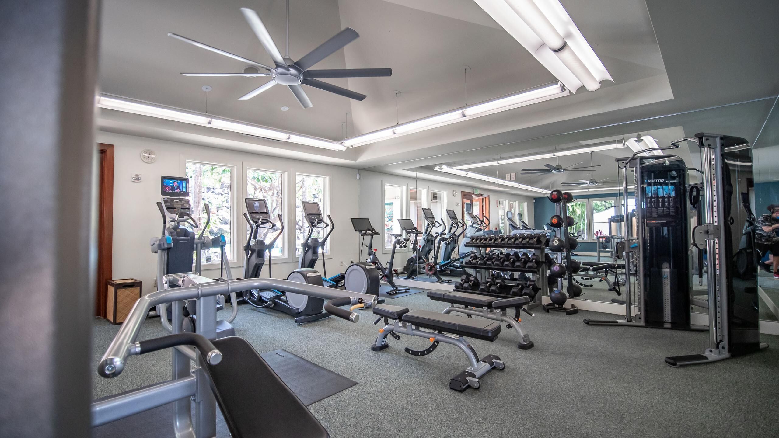 Une salle de sport équipée de tapis de course, de vélos elliptiques, de poids libres et d’une machine de musculation.