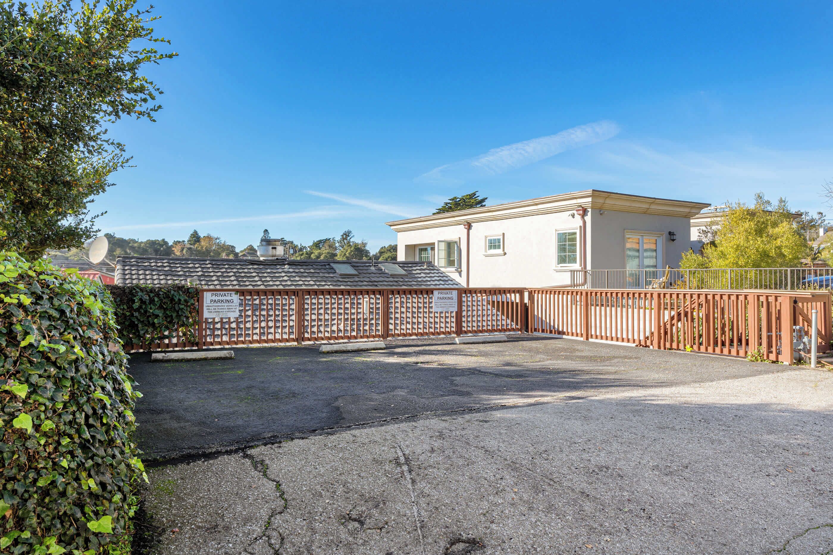 A private parking area with a gated entrance, a building with a flat roof, and a clear blue sky.