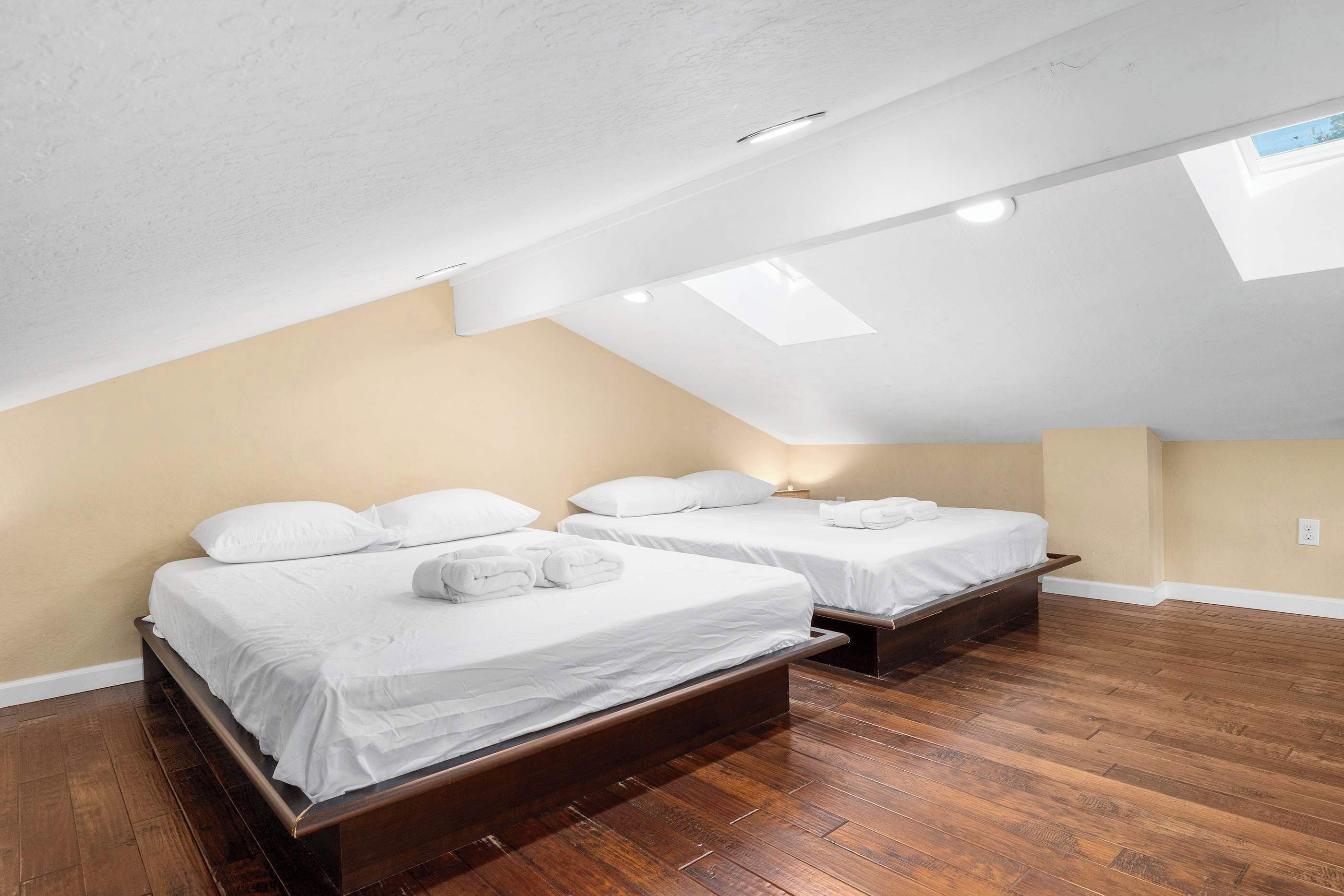 Una habitación con dos camas, suelo de madera y techo inclinado con tragaluces.